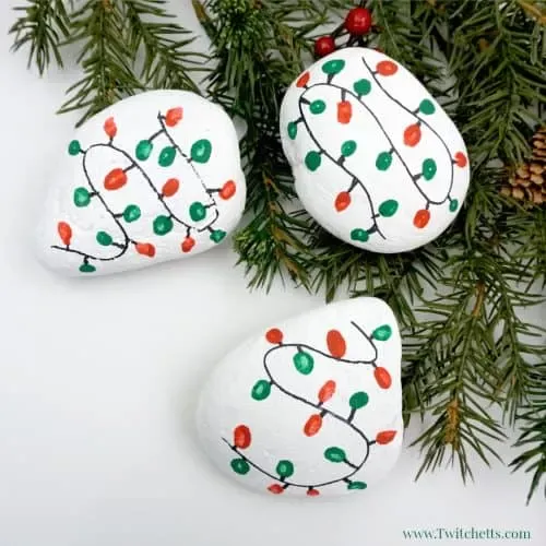 This Christmas lights rock art is easy, fun, and a perfect painted rock to give as a gift or hide in your nearest park. #christmas #rocks #christmaslights #rockpainting #stonepainting #rockpaintingideasforkids #stockingstuffer #christmasartproject #fingerprint #twitchetts