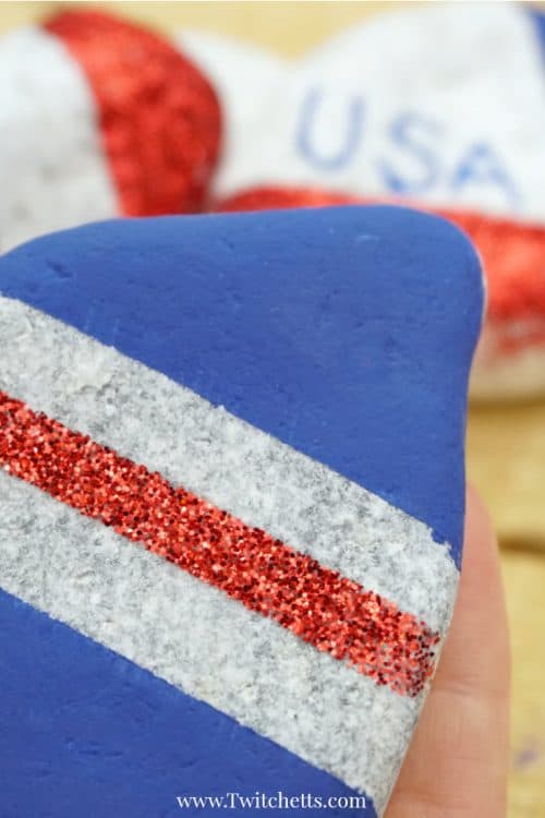 Create these amazing patriotic rocks that sparkle and shine with pride. This rock painting idea for kids is perfect for hiding around town and showing off those red, white, and blues. #patrioticrocks #4thofjuly #independenceday #usa #america #rockpaintingideasforkids #glitter #craftsforkids #artprojectsforkids #twitchetts