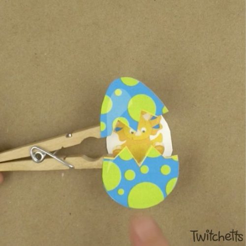 This hatching dinosaur egg craft  is lots of fun and a great craft for preschoolers. Grab our template and a couple of simple craft supplies and you have a fun craft that your child will want to play with! #hatchingdinosaureggcraft #dinosaur #egg #hatching #craftforkids #clothespin #template #twitchetts