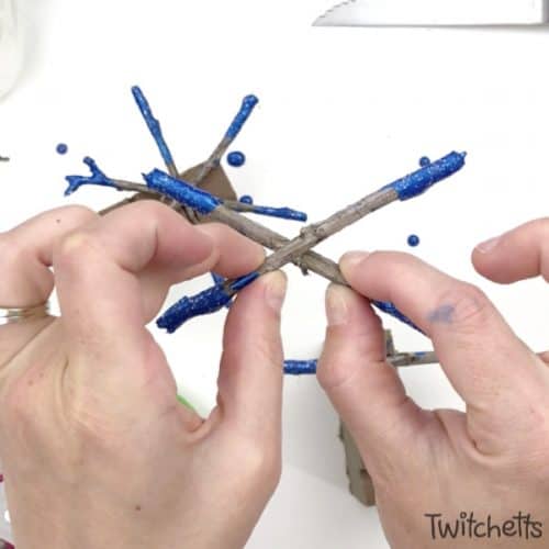 Create beautifully dipped twig snowflake ornaments using sticks from your yard! This is a great handmade ornament that kids can help create. #snowflakeornament #twigornament #twigsnowflake #christmasornaments #kidscrafts #christmascraft #classroomcraft #nature #giftsfromkids #twitchetts