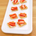Image of cheesecake bites topped with strawberries. Text reads "Easy Party Dessert. Cheesecake Bites"